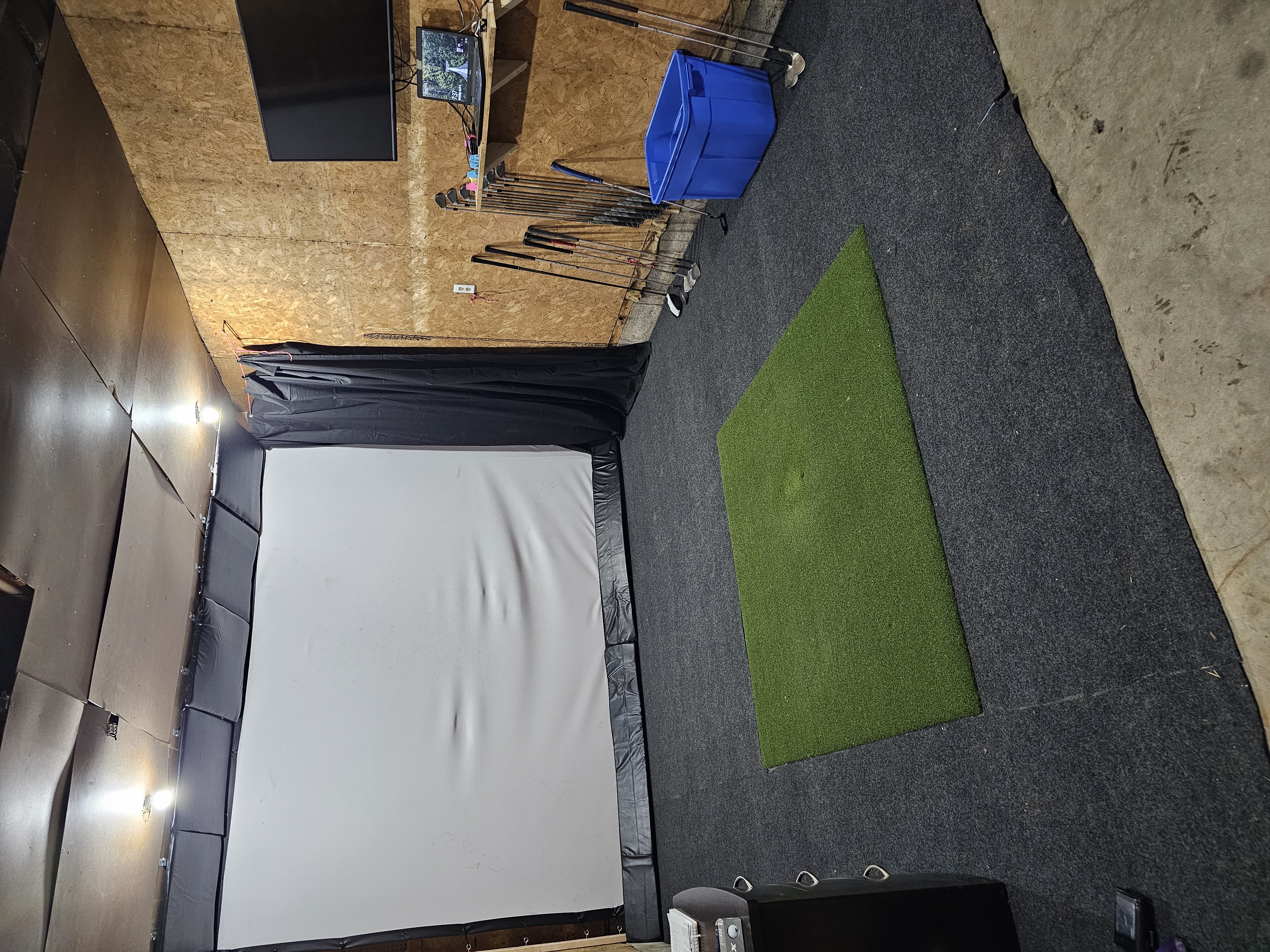 Finished garage golf simulator bay with impact screen, projector, mat, and lighting